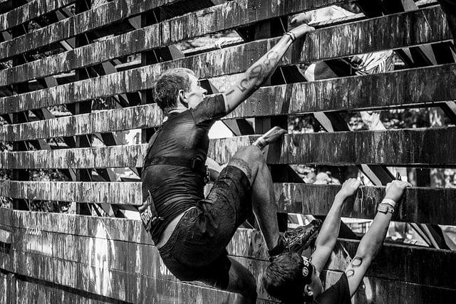 A man training for an obstacle race, dominating a wooden wall in a black and white photo.