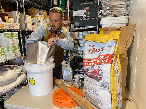 A man with a bucket in front of a shelf full of budget survival food.