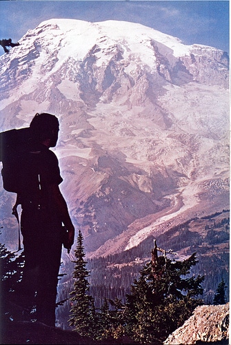 A man is embarking on an ultra-backpacking adventure, skills in hand, standing triumphantly on top of a mountain with a backpack.