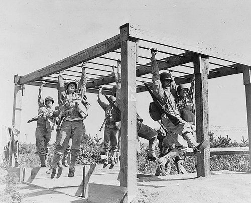 A group of fit GIs hanging from a wooden structure during World War II.