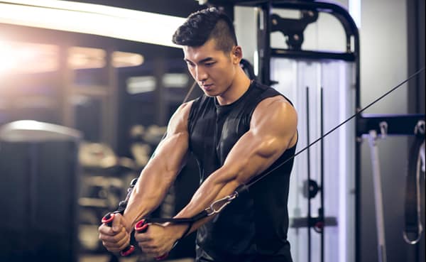 A person in a gym using a cable machine for strength training, performing a chest exercise with focused expression, showcasing the efficacy of cable machine workouts.