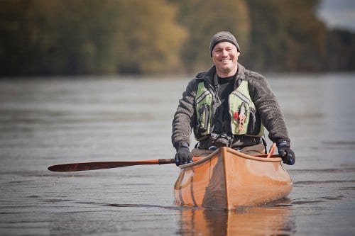 An outdoor shop owner is paddling a canoe in a river.