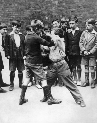 A black and white photo depicting a group of boys engaged in a spirited fight.