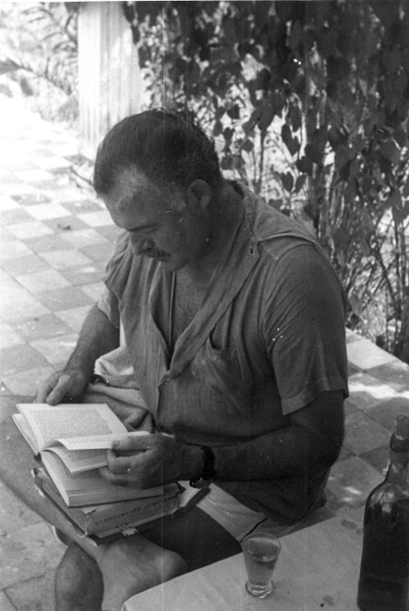 Ernest Hemingway is reading book outside at table.