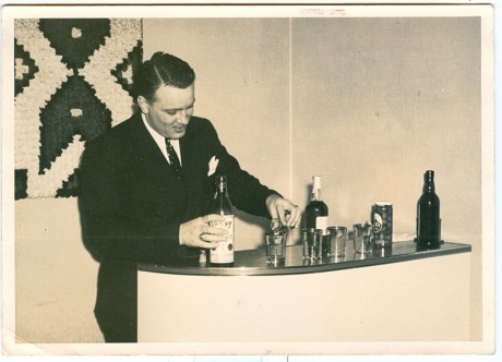 A stock image of a man in a suit pouring a bottle of wine at his home bar.