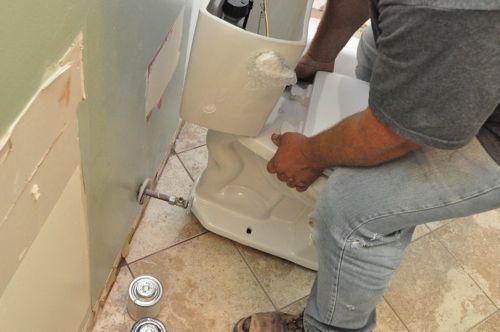 A new toilet setting toilet seat onto closet bolts and wax ring.