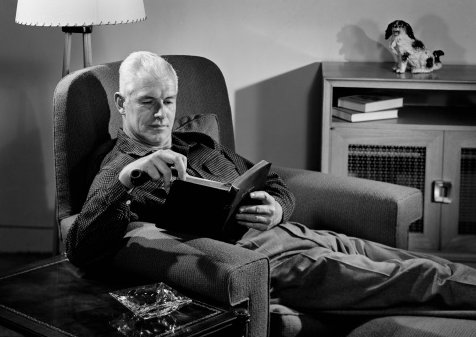 A man engrossed in a fiction book, reading while comfortably seated in a chair.