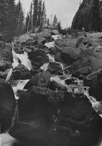 A minimalistic black and white photo showcasing the manliness of a waterfall nestled amidst mountainous landscapes.