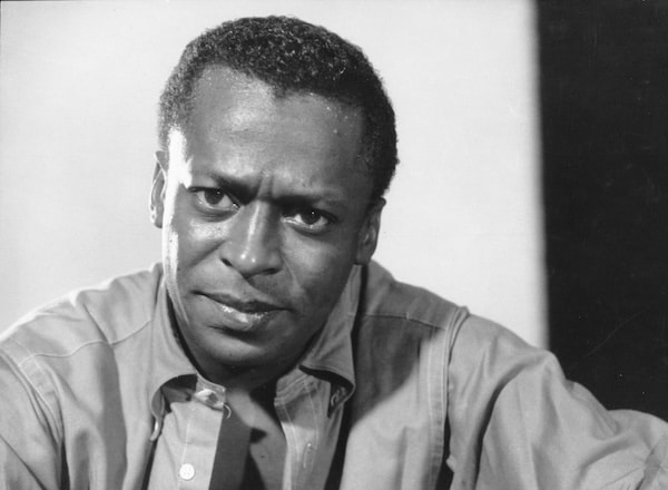 Black and white photo of a man with short hair, wearing an OCBD shirt buttoned up, looking directly at the camera with a serious expression.