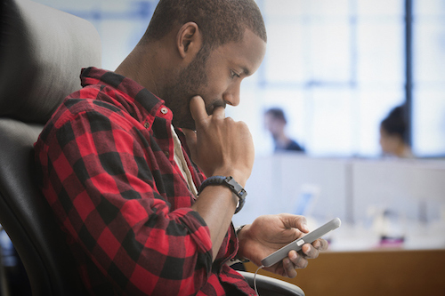 A man sitting in an office chair texting on his cell phone.