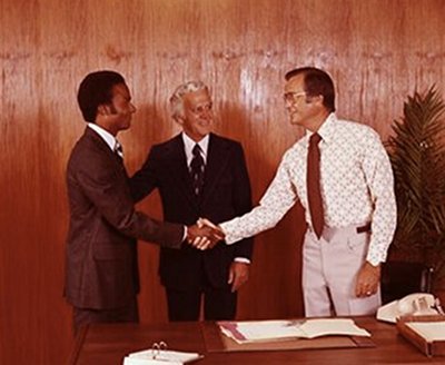 Three men shaking hands in front of a desk, sealing a successful selling deal with an effective pitch.
