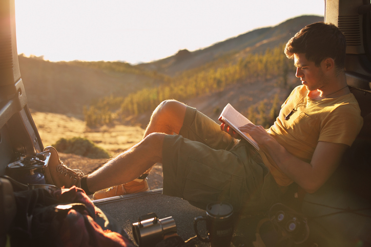 A man sitting in the back seat of a car reading for pleasure.
