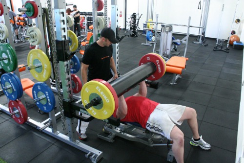 Ryan Martens lifting a weight while laying with a trainer.