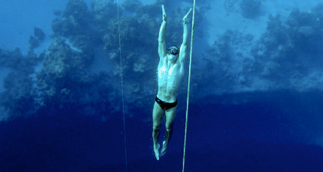 A man is hanging from a rope in the deep sea.